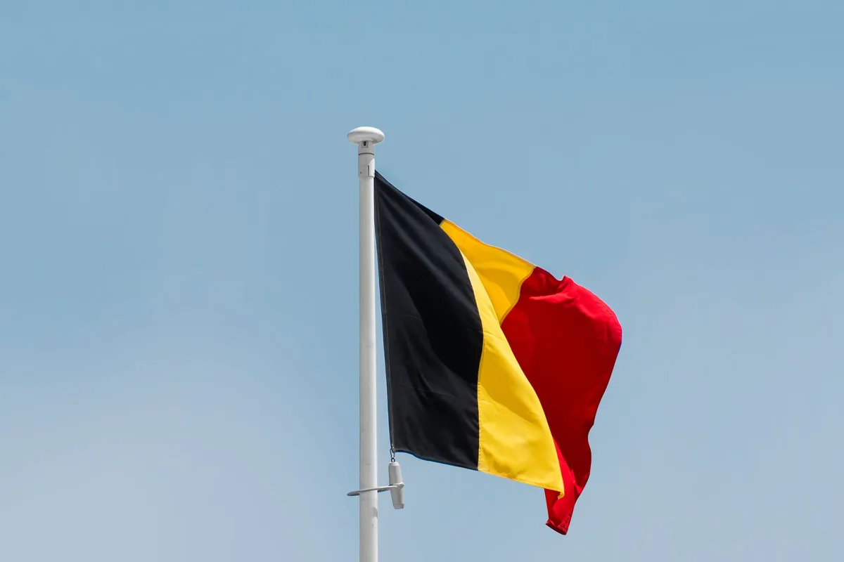 Drapeau belge noir, jaune et rouge flottant sur un mât, sous un ciel bleu, à Bruxelles